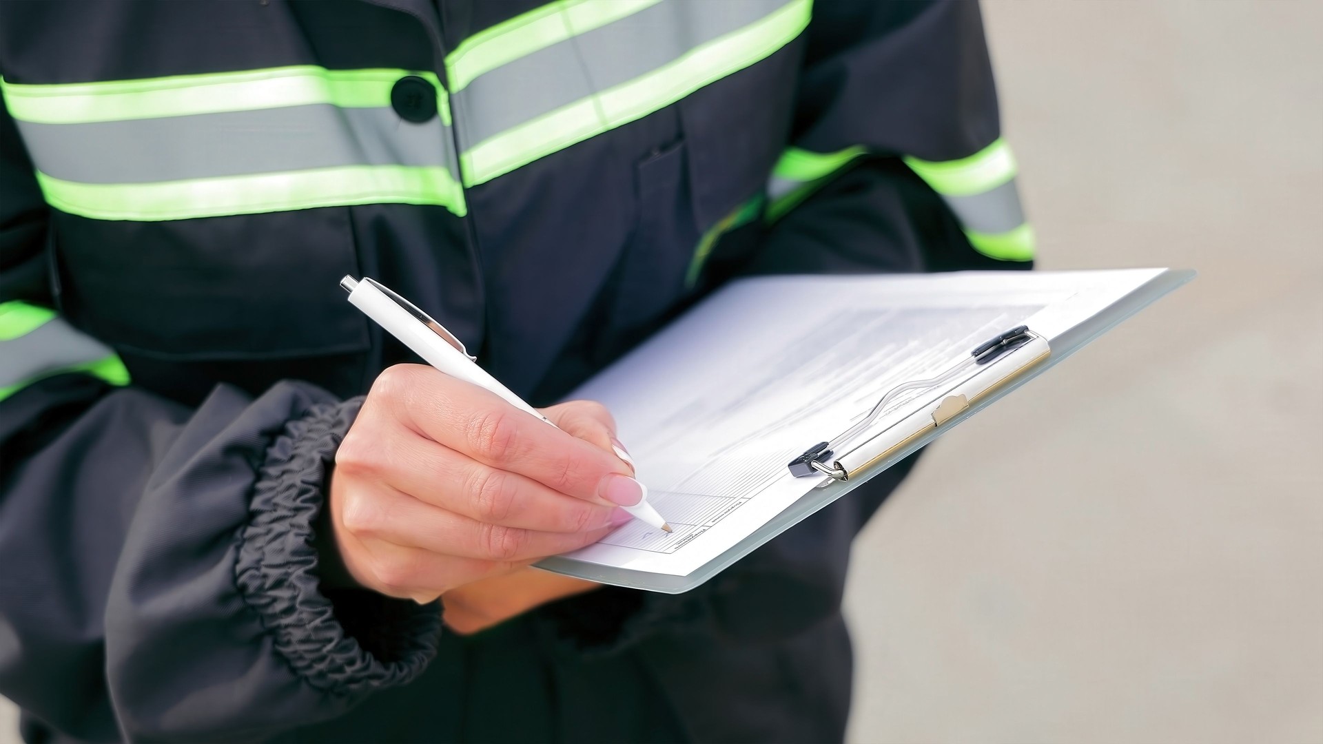 Worker Writing on Clipboard for Inspection. Close-up of a worker in reflective safety gear writing on a clipboard, documenting information during an inspection or checklist process.